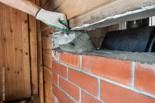 Bricklayer lays red brick around a sauna stove using a trowel. This is renovation work. The bricks are laid on a refractory sand-cement mixture.