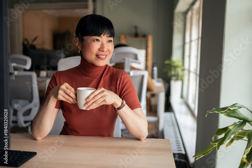 Smiling Woman Enjoying Coffee at a Bright Office Desk