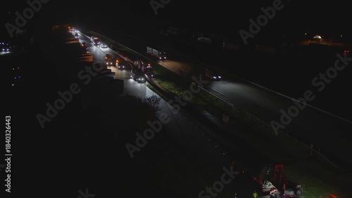 Spectacular heavy transport of a wind turbine rotor blade at night on a multi-lane highway. The oversized truck is illuminated by escort vehicles on the dark road.