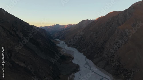 Aerial view captures a river gracefully winding through majestic mountains at dawn, showcasing the serene landscape and soft morning light, camera pans smoothly to reveal more of the scene
