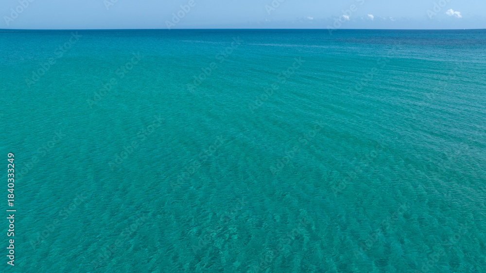 Obraz premium Aerial view of the crystal clear, turquoise sea. The sea stretches to the horizon with colours ranging from azure to dark blue. Ideal for concept of tropical seas. Sunny summer morning. 