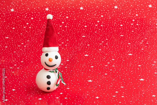 Happy little handmade snowman with Santa hat on red background with white stars and copy space