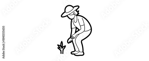 A person in a hat is bending over to tend to a small plant with care and attention to detail outdoors
