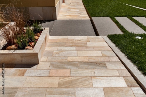 Contemporary outdoor design with beige limestone tiles, concrete inserts, and grass—clean lines and material contrast.