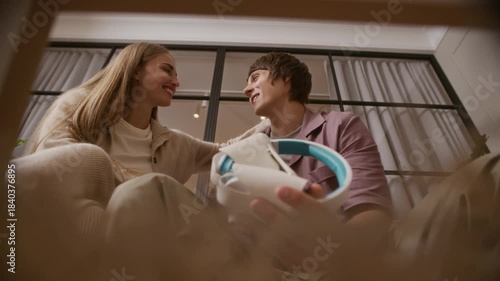 From-inside-box shot of young Caucasian man kissing his girlfriend after receiving new headphones as present, sharing joyful and affectionate moment together in cozy home interior
