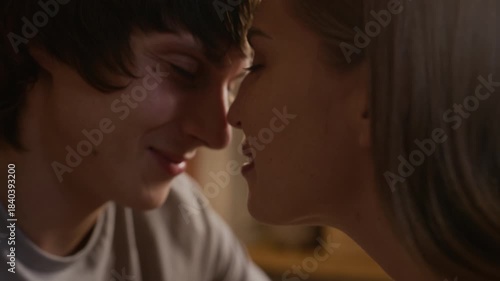 Closeup of affectionate young Caucasian couple sitting close together, kissing tenderly and sharing warm and intimate moment while enjoying each other closeness and romantic connection