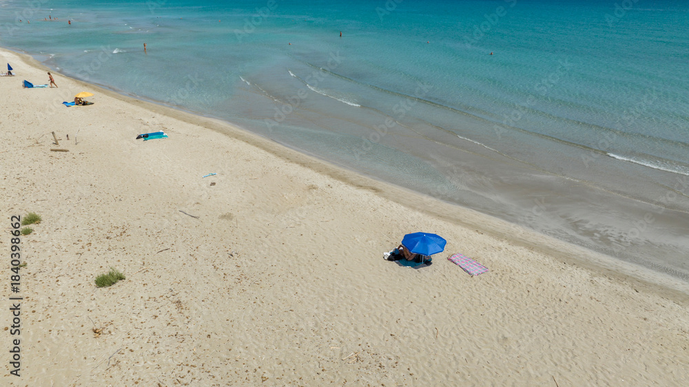 Obraz premium Aerial view of a beautiful sandy beach overlooking a turquoise and crystal clear sea. Beach umbrellas of tourists at San Lorenzo Beach in the Province of Syracuse, Sicily, Italy. Sunny summer morning.
