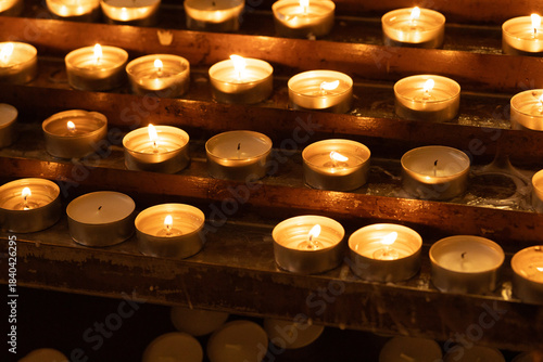 Rows of glowing candles inside a Catholic church, lit for prayer, remembrance, and commemoration of loved ones. The warm candlelight creates an atmosphere of peace, spirituality, and hope.