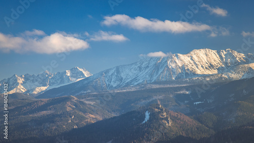 Fototapeta Naklejka Na Ścianę i Meble -  Tatra Mountains above Zakopane town in Poland, Europe. Panoramic views of a rugged mountain range with snow-dusted peaks under a bright blue sky, a tranquil and majestic landscape.