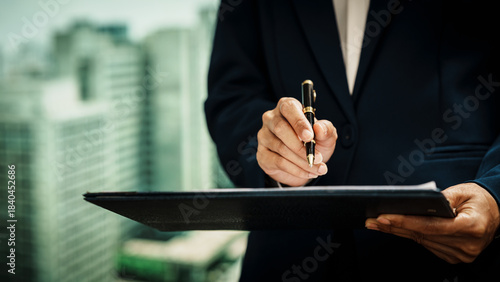 Business professional writing on clipboard with pen against an urban skyline, documentation, corporate workflow, decision-making,  modern professional responsibilities in a city business environment.