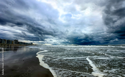 Nieuwpoort, West-Vlaanderen, Belgium, Ocotber 25th, 2025, rough waves crashing onto shoreline under heavy storm clouds with foamy surf carving wet sand, dark blue tones, atmospheric
