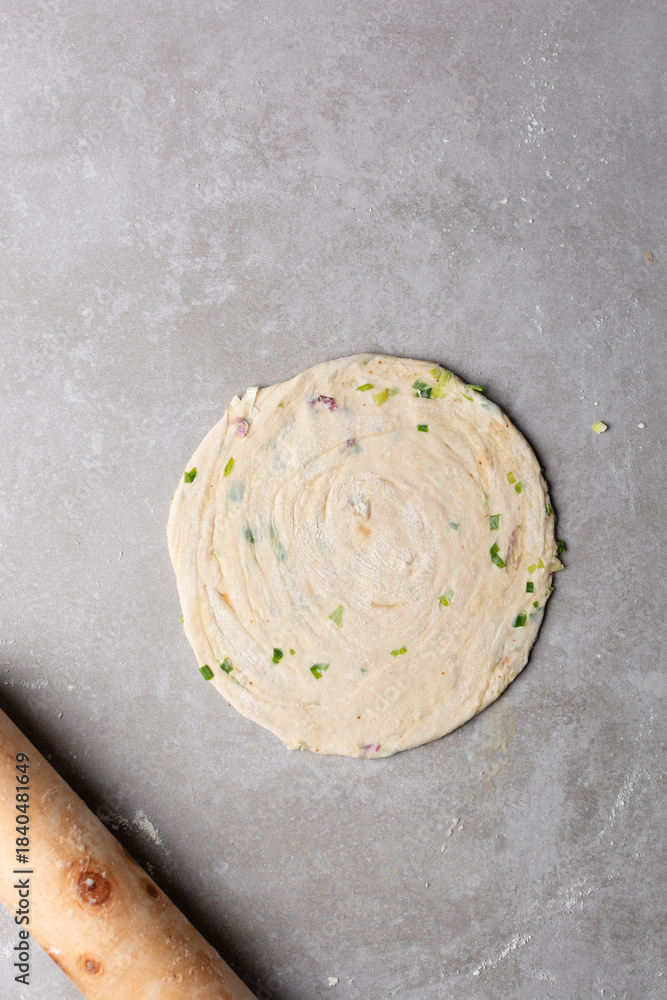 Obraz premium Overhead view of rolled out raw chinese scallion pancakes on a white plate, top view of homemade scallion pancakes, process of making cong you bing