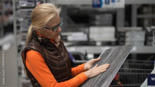 Mature woman holds a tile sample in a bright hardware store while looking for materials for home improvement projects