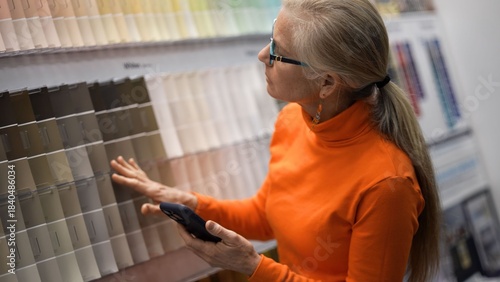 Mature woman looks at color samples in a hardware store while planning for home renovation projects with her phone in hand