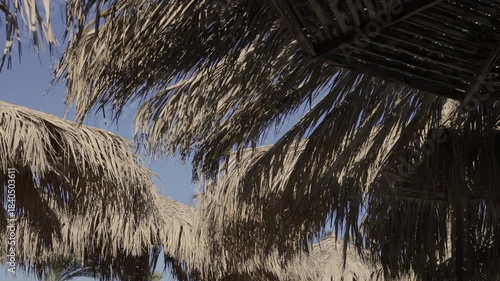 Close-up view of a traditional thatched roof made from dried palm leaves against a clear blue sky. Slow motion.