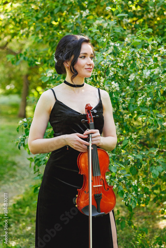 Elegant musician posing with violin in a lush garden