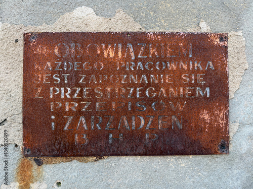 Rusty metal safety sign with a message reminding that every employee is required to follow workplace health and safety regulations. polish text