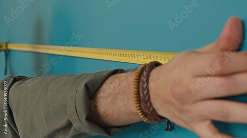 Extreme close-up shot of hands of unrecognisable man measuring length of teal wall with tape measure