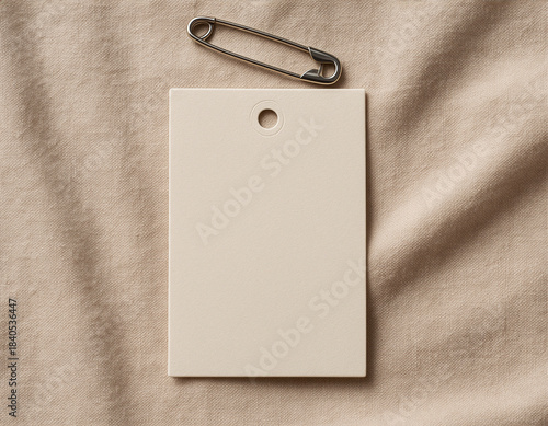 Beige rectangular clothing price tag mockup with safety pin on fabric background