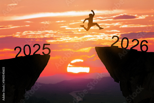 Silhouette of a brave man jumping from the cliff 2025 to 2026 against a sunset sky. Concept of New Year, success, challenge, and moving forward to the future.