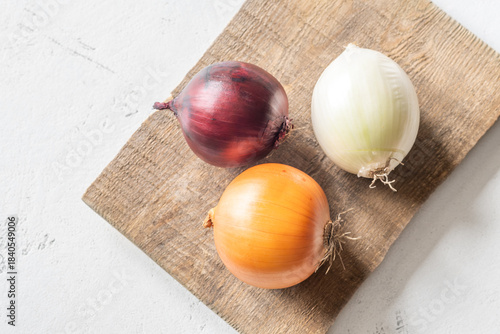Three whole onions on rustic board showing red, yellow, and white varieties