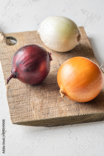 Three whole onions on rustic board showing red, yellow, and white varieties