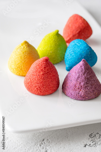 Colorful sugar-coated marshmallow pyramid candies sparkling on clean white rectangular platter