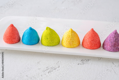 Colorful sugar-coated marshmallow pyramid candies sparkling on clean white rectangular platter