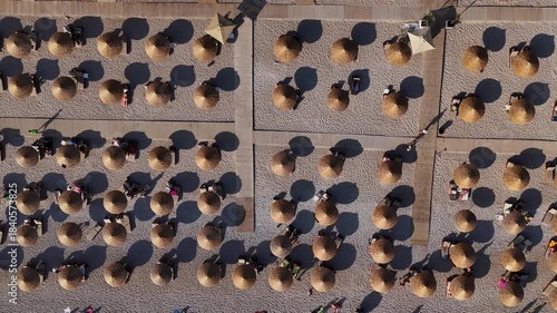 Top view of sandy beach with sun umbrellas and tourists resting in Kas, Turkey. Summer seaside vacation scene with people relaxing on sunbeds by the Mediterranean Sea.