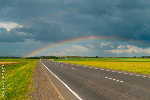 Fotografija a rainbow over the road in the middle of green summer fields
