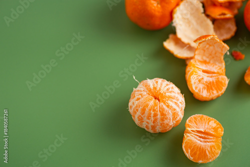Fresh mandarins and peeled citrus segments on green backdrop