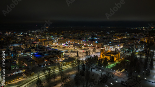 Aerial view of a snow-dusted cityscape, where golden lights illuminate a prominent building amidst the dark, wintry night, Joensuu, North Karelia, Finland.