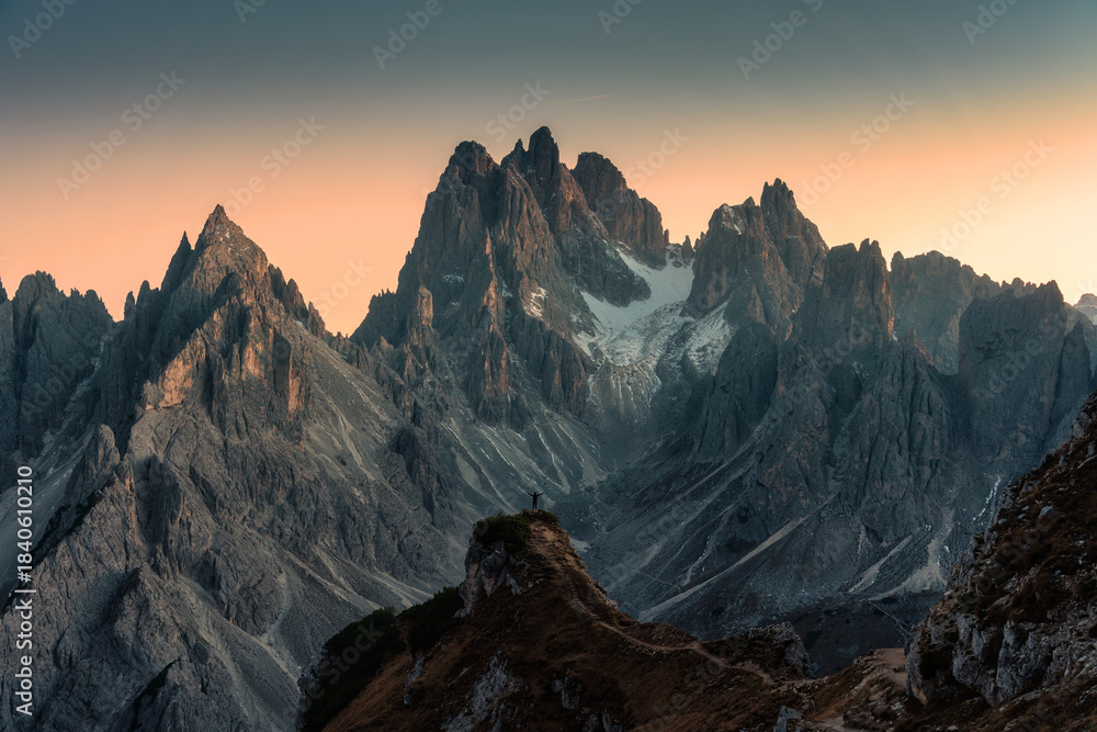 Obraz premium Alpine landscape of Cadini di Misurina with rugged mountain peak and male tourist hiking during sunset in Dolomites, Italy