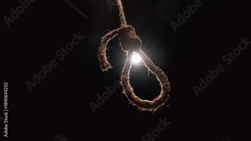 Sinister hangman's noose made of thick jute rope swinging slowly in a dark, scary room with a single spotlight in the background, symbolizing death, despair, and capital punishment
