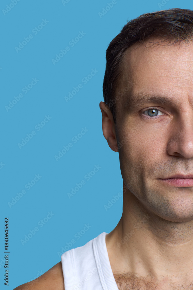 Obraz premium Portrait of Caucasian middle aged man looking at camera with serious expression, closeup of face and upper torso against blue background, short brown hair visible