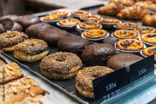 Tablou pe pânză Bakery Display Case with Chocolate Donuts and Portuguese Egg Tarts