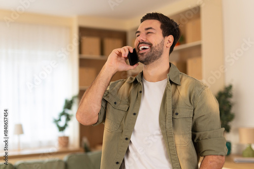 Tableau sur toile Young man happily talking on mobile phone at home