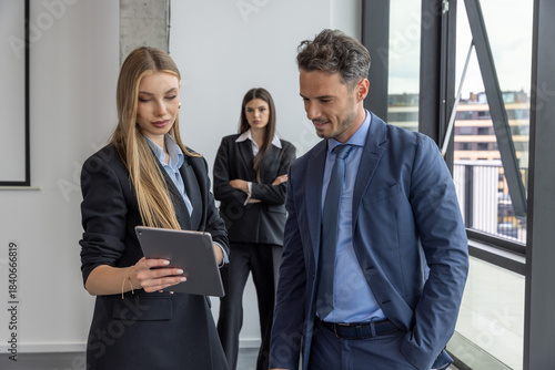 A jealous businesswoman observes a conversation between two colleagues.