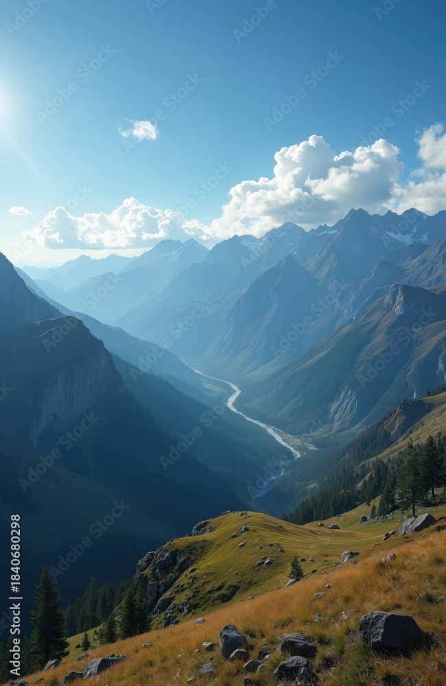 Fototapeta premium Vast mountain valley with winding river below, green hillsides, and clear blue sky overhead. Tall peaks recede into haze, sun shines brightly.