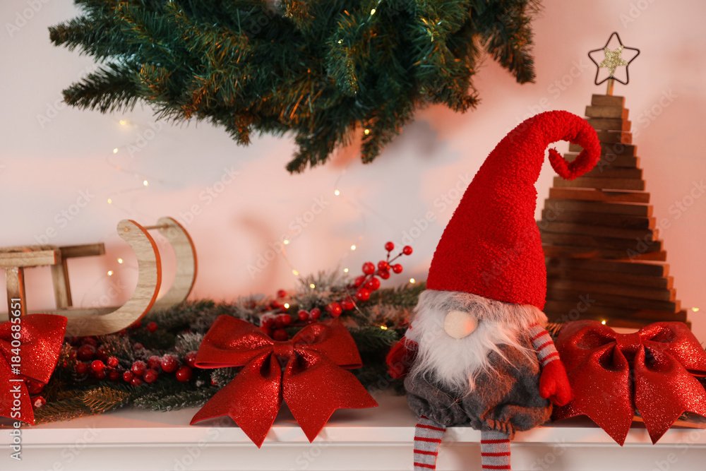 Naklejka premium Cute Christmas gnome and decor on shelf near white wall indoors