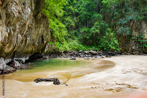 Emerald Cave's hidden sandy beach and clear green water are enclosed by towering limestone cliffs covered in lush tropical foliage, creating a serene and secluded natural escape in Kantang, Trang