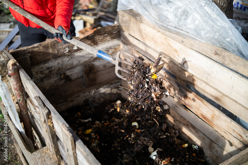 Turning Compost with a Garden Fork in a Wooden Compost Bin