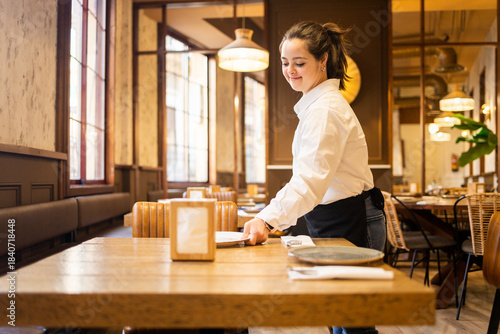 A young woman between 20 and 30 years old with Down syndrome is working as a waitress in a cafeteria.The girl is placing a plate on the table. Concept of trisomy 21.