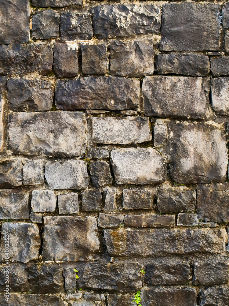 Obraz premium A wall made of stone with moss growing on it. The wall is gray and brown in color. Background for design, Stone mason craft.