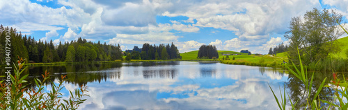 Grosses Panorama in der Nähe der Ortschaft “Seeg im Allgäu“ mit einem Teich im Vordergrund.