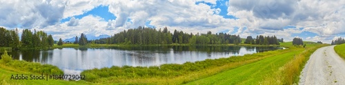 Grosses Panorama in der Nähe der Ortschaft “Seeg im Allgäu“ mit einem Teich im Vordergrund.