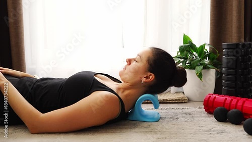 Young woman lies on the floor using a blue cervical traction device to stretch the neck. Home therapy for neck pain, muscle tension and spine decompression.