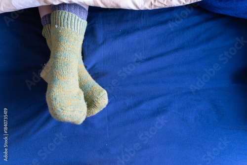 Warm wool socks resting on a blue bed sheet, cozy home comfort and relaxing morning atmosphere.