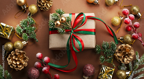 Christmas ornaments and handmade gift box with bow, decorative fir branch, glittering balls and golden cones for tree decoraton. New Year winter holiday composition with presents, decor, top view.