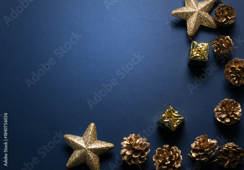 Christmas minimalistic dark blue background with decorative glittering stars, golden gift box and cones for tree decoraton. New Year winter holiday composition with decor and space for text, top view.